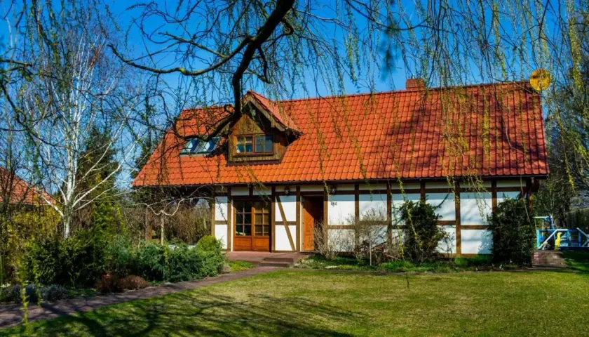 Urokliwy dom z czerwonym dachem, otoczony zielenią. Idealne miejsce na luksusową agroturystykę, gdzie można odpocząć od miejskiego zgiełku.