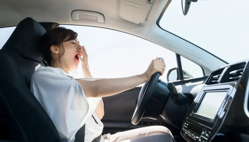 Mujer bostezando al conducir mucho tiempo sin descansar. El cansancio al volante es peligroso.