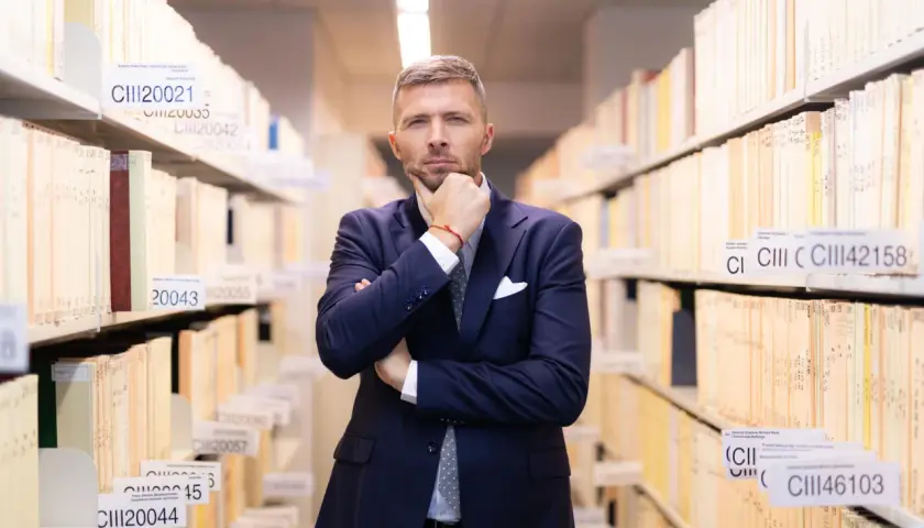 Mężczyzna w garniturze zastanawia się, jak liczyć 6 miesięcy na odrzucenie spadku, wśród regałów pełnych akt.