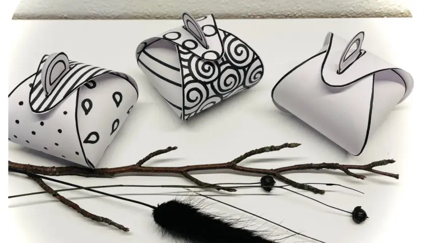 Drei selbstgebastelte Geschenkboxen mit Mustern, inspiriert von Vorlagen zum Geschenkbox selber basteln. Ein Ast und schwarze Federn liegen daneben.