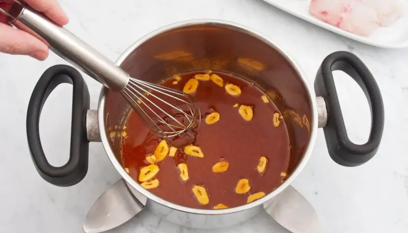 Batir salsa con ajo en una olla. En un plato, trozos de rape fisch listos para cocinar.