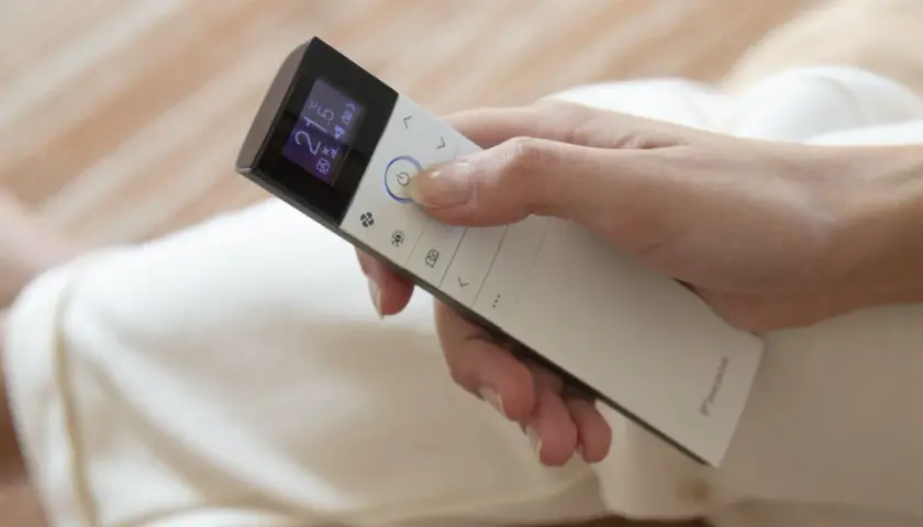 Mano ajustando el aire acondicionado a 21 grados. El mando muestra el modo "cool" para un ambiente fresco.