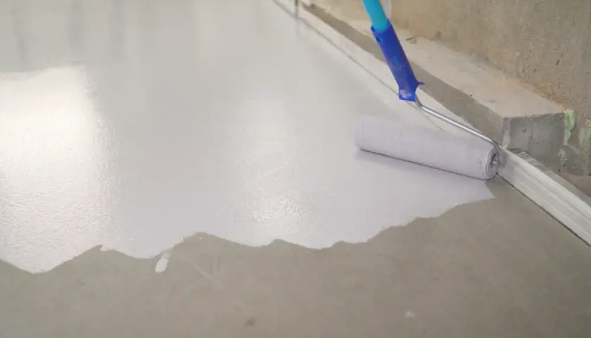 Wałek maluje beton na biało, tworząc gładką, jednolitą powierzchnię.
