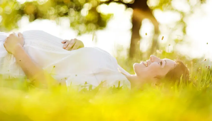 Une femme enceinte, baignée par le soleil, sourit en se prélassant dans l'herbe verte.