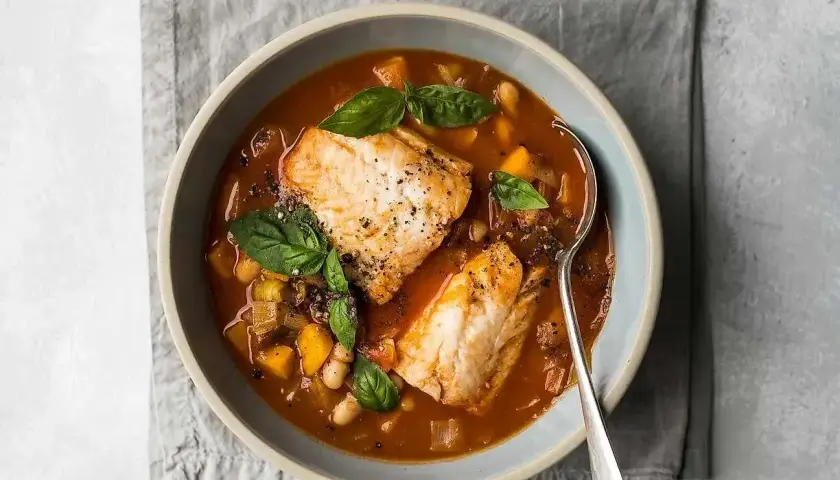En skål med mustig fisksoppa med vita bönor, grönsaker och färsk basilika. Ett perfekt fisk recept för en kall dag.