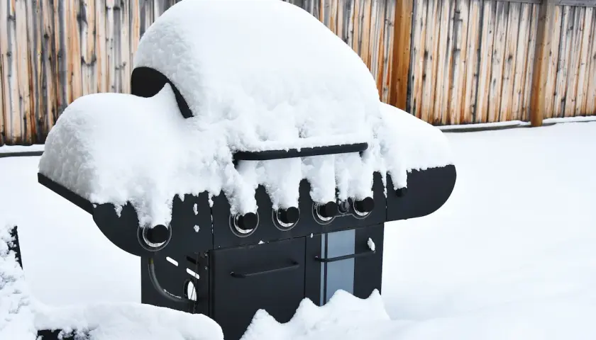En snötäckt gasolgrill under tak, redo för sommarens grillkvällar trots vinterns kyla.