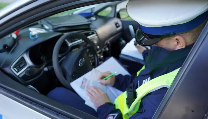 Policjant w radiowozie spisuje mandat za jazdę bez kasku.