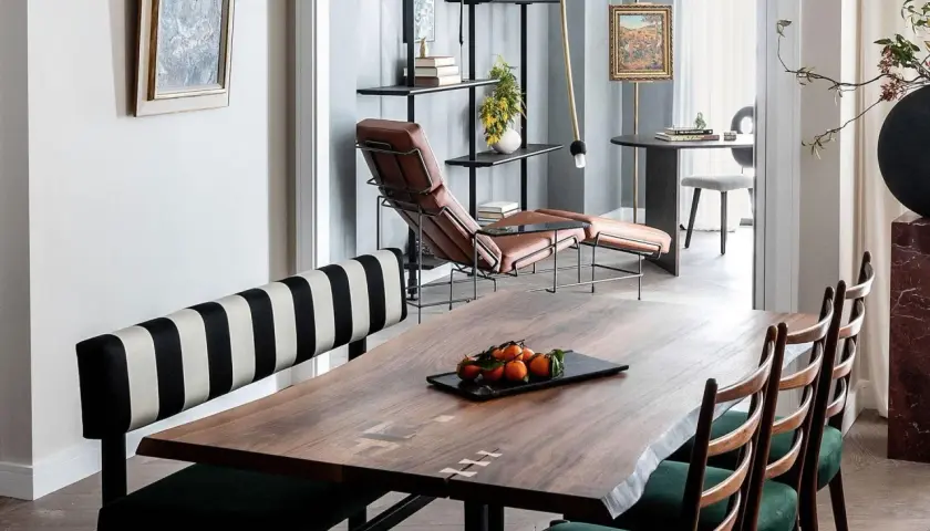 A large, live-edge wooden table with inlaid details, showcasing its impressive table dimension, is set with a tray of tangerines.