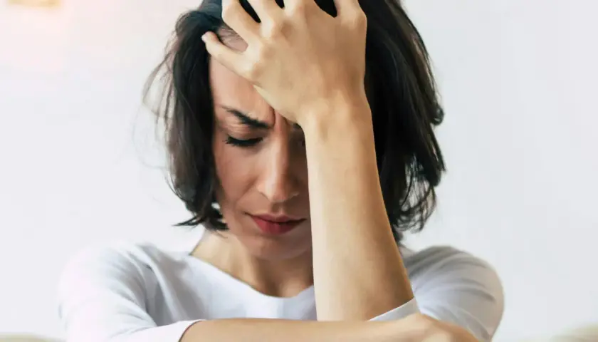 En kvinna med handen mot pannan, ansiktet nedåt, visar tydliga tecken på depression och dess fysiska symptom som huvudvärk och utmattning.