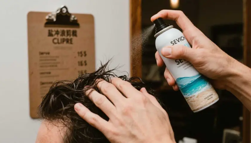 Un hombre aplica spray sal marina pelo para un look playero.