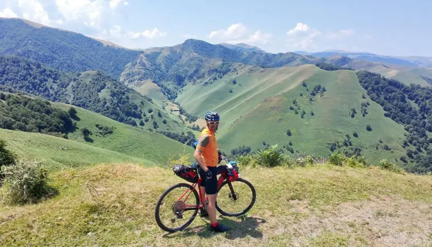 Ciclista con su bicicleta de gravel en un paisaje montañoso verde, disfrutando de la ruta transpirenaica.