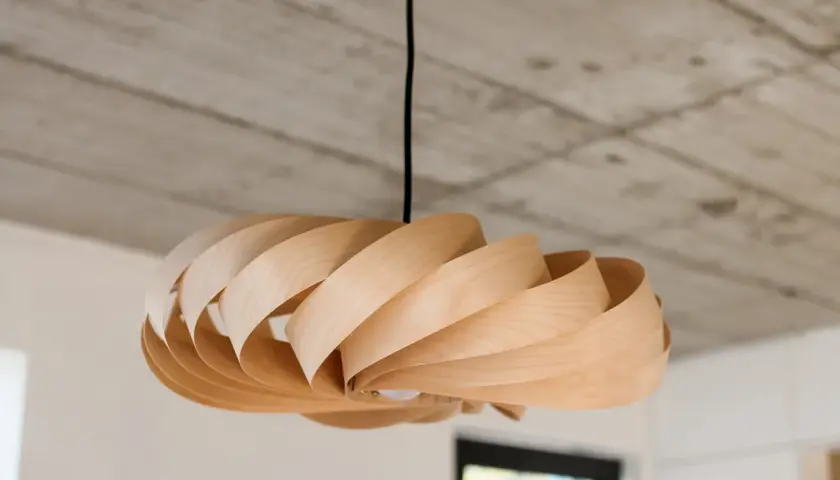 Drewniana lampka DIY o spiralnym kształcie, zawieszona pod betonowym sufitem.