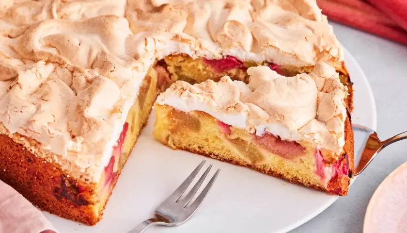 Saftiger Rhabarberkuchen mit luftigem Baiser, ein Stück ist schon angeschnitten.