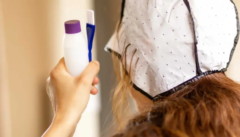 Persona se prepara para hacerse mechas en casa. Sostiene un kit para teñir el cabello y lleva un gorro especial.