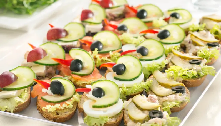 Kolorowe kanapki na talerzu, idealne na pan kanapka catering. Różne dodatki: łosoś, jajko, ogórek, oliwki, winogrona.