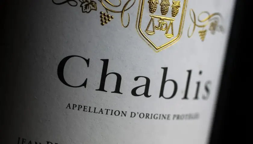 Gros plan sur une étiquette de vin Chablis, avec un blason doré orné de grappes de raisin et d'une balance. L'appellation d'origine protégée est clairement visible.