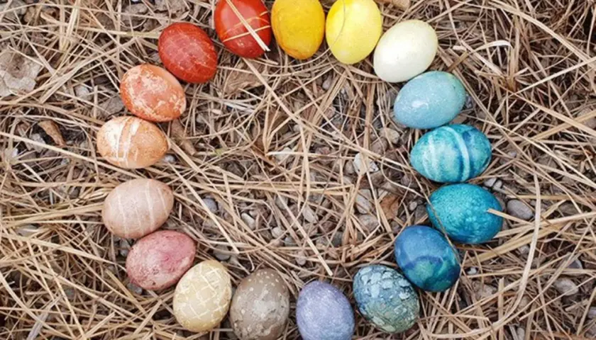 Bunte Ostereier, darunter auch einige braune Eier, bemalen und kunstvoll arrangiert auf trockenem Gras und Steinen.