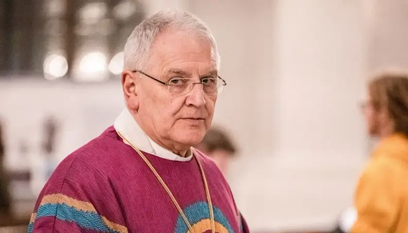 Bischof Heinrich Timmervers trägt ein violettes Messgewand mit bunten Streifen. Er blickt ernst in die Kamera.