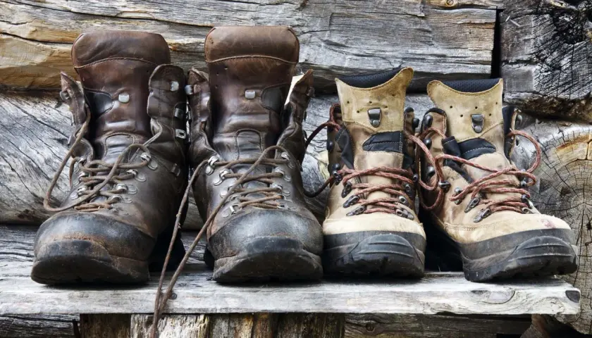 Four pairs of hiking boots, two dark brown leather and two tan, sit on a wooden shelf. Considering if you should size up in hiking shoes?