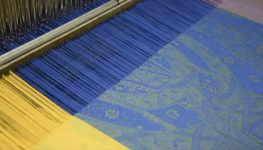 Le métier à tisser jacquard crée un motif complexe sur un tissu bleu et jaune.
