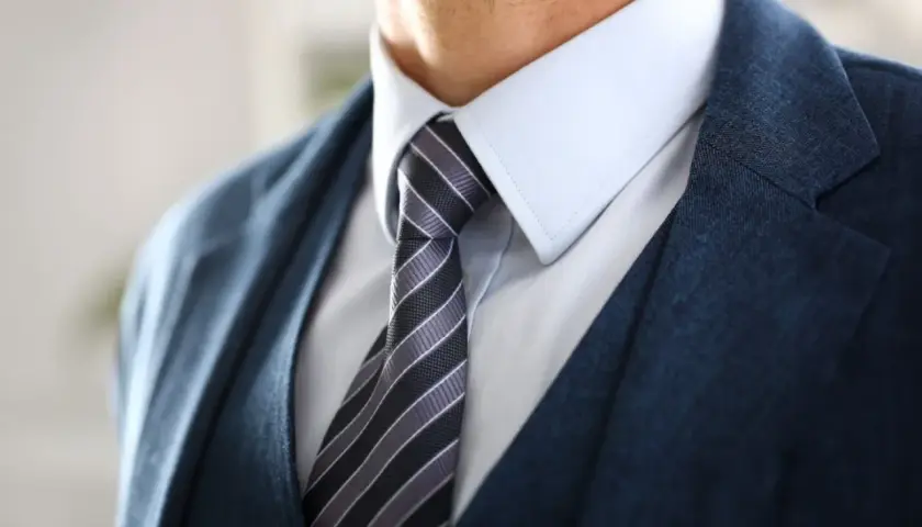 Zbliżenie na męski garnitur z granatową marynarką, jasnoniebieską koszulą i krawatem w paski.