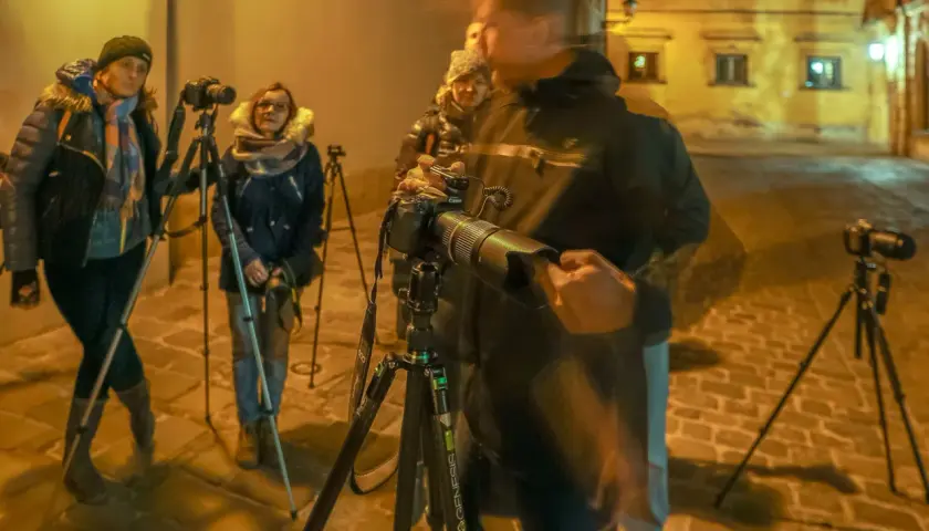 Uczestnicy kursu fotografii dla początkujących ćwiczą nocne zdjęcia na brukowanej uliczce.