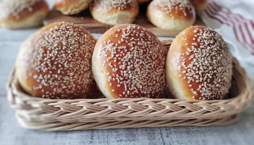 Świeżo upieczone bułki do burgerów, posypane sezamem, w wiklinowym koszyku. Idealne na domowe burgery.
