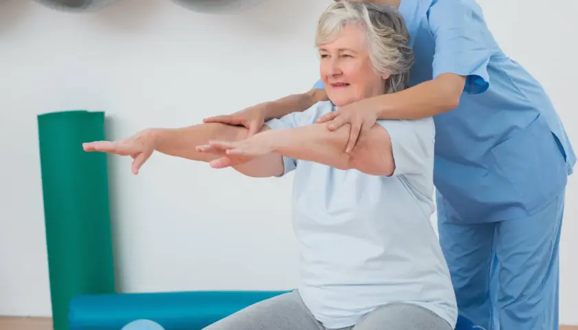 Terapeuta ayuda a una mujer mayor con ejercicios de movilidad sentada en una pelota de ejercicio.