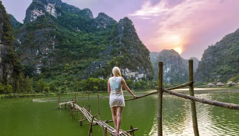 Frau auf Bambusbrücke in Vietnam, umgeben von Karstbergen und einem See. Tolle Reise-Hacks für unvergessliche Momente.