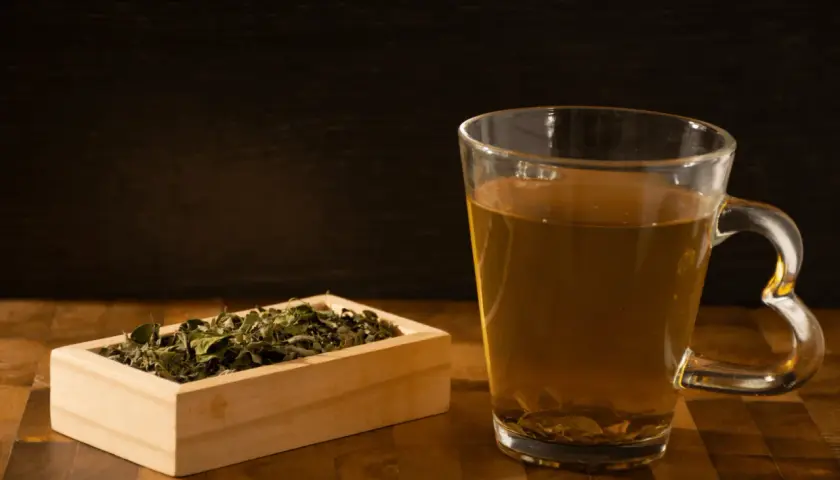 Herbata moringa, znana z właściwości leczniczych, w szklance i drewnianej skrzynce z suszonymi liśćmi.