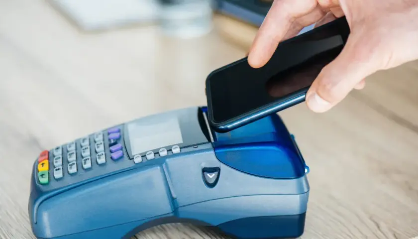 Zbliżenie na dłoń zbliżającą smartfon do terminala płatniczego. Szybka płatność za zakupy, nawet gdy używasz gruzińskiej waluty.