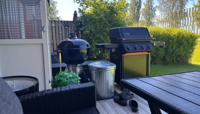 En Weber kolgrill bäst i test står redo för sommarens grillkvällar bredvid en gasolgrill. Trädgårdsmöbler och en fin gräsmatta skapar en härlig atmosfär.
