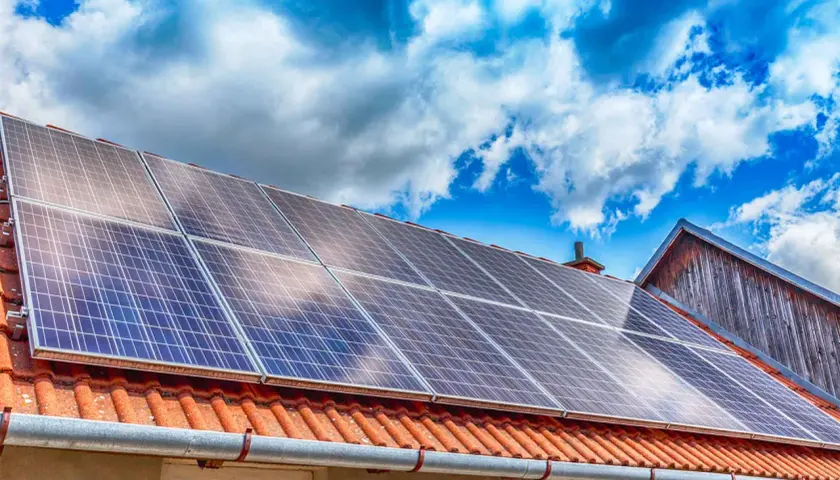 Panneaux solaires sur un toit de tuiles rouges sous un ciel bleu et nuageux. Une installation qui peut influencer le coût de l'assurance photovoltaïque.