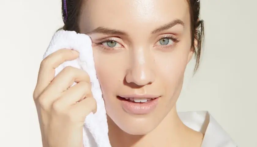 Mujer con toalla blanca limpiando su rostro, evitando el maquillaje cuarteado.
