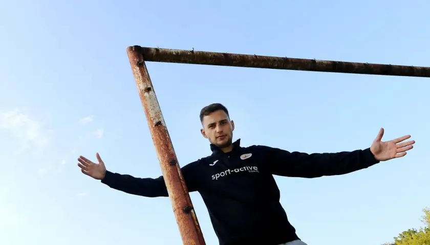 Młody piłkarz z Częstochowy, w czarnej bluzie z logo "sport-active", pozuje na tle nieba i zardzewiałej poprzeczki bramki.