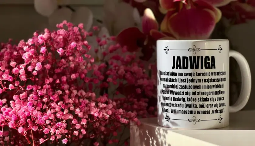 Kubek z napisem "Jadwiga" i opisem imienia, otoczony delikatnymi, różowymi kwiatami. Idealny prezent na imieniny Jadwigi.