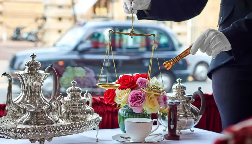 En elegant uppsättning för klassisk afternoon tea med silverkannor, en blomsterbukett och en våg för att mäta teblad.