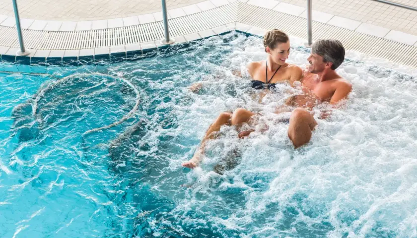 Para relaksująca się w jacuzzi, para uśmiecha się do siebie.