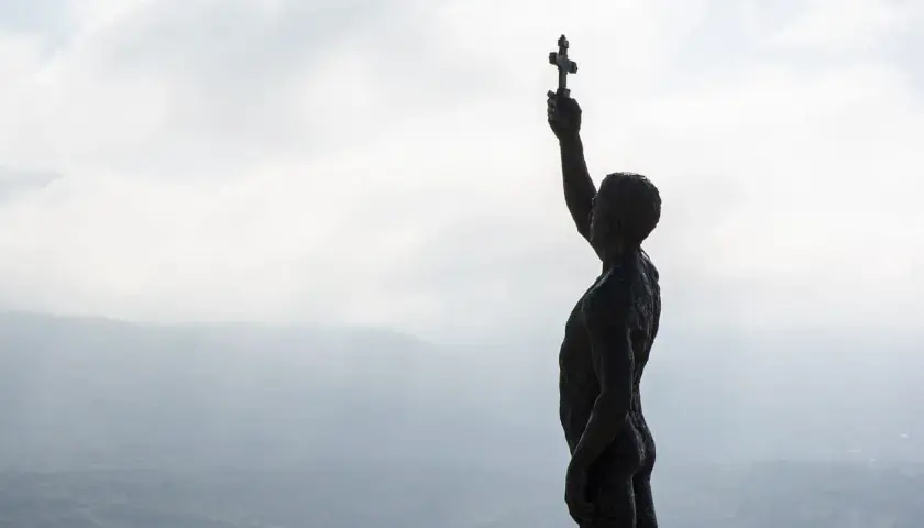Sylwetka postaci z krzyżem wzniesionym ku niebu, jakby w nadziei na koniec trzech dni ciemności.