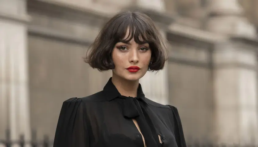 Mujer con un elegante corte de pelo **french bob**, labios rojos vibrantes y un top negro con lazada.