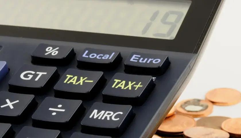 Kalkulator z klawiszami "TAX+", "TAX-" i "Euro" obok stosu monet. Czas na rozliczenie działalności gospodarczej do kiedy?
