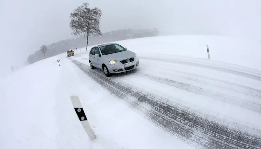 Coches circulando por carreteras con nieve en un día de invierno con poca visibilidad.