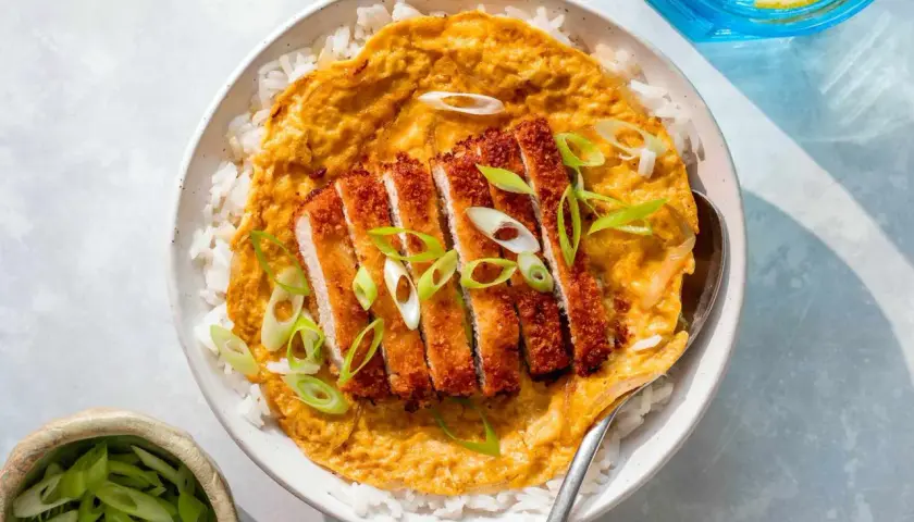A delicious katsu don with crispy pork cutlet over rice, topped with a savory egg mixture and garnished with fresh scallions.
