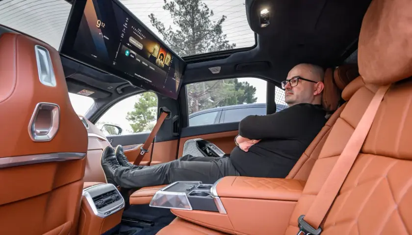 Wnętrze BMW i6 z ekranem multimedialnym dla pasażerów. Mężczyzna relaksuje się na tylnym siedzeniu.