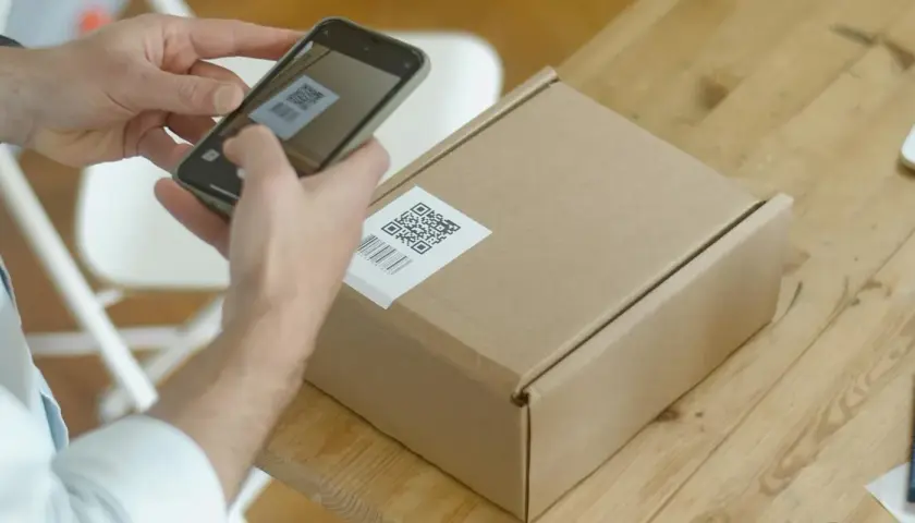 Ręce skanują kod QR na paczce, przygotowując ją do wysyłki w ramach dropshippingu.
