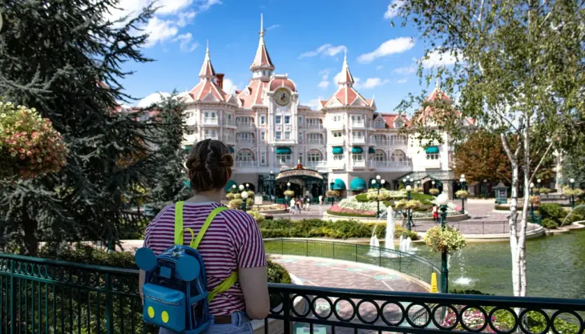 Dziewczyna z plecakiem w kształcie Myszki Miki patrzy na zamek w Disneylandzie. Zastanawia się, ile kosztuje bilet do Disneylandu.