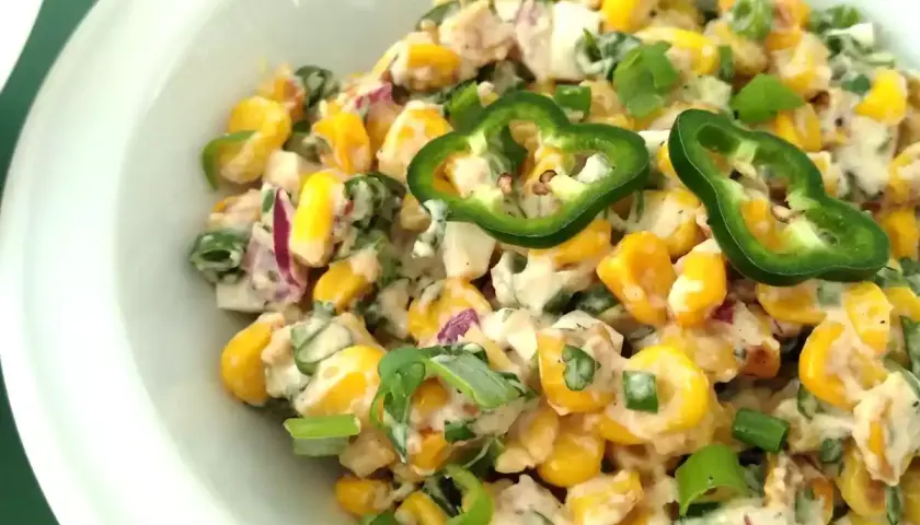 Deliciosa ensalada de maiz cremosa con jalapeños, cebolla morada y cebollín, servida en un tazón blanco.