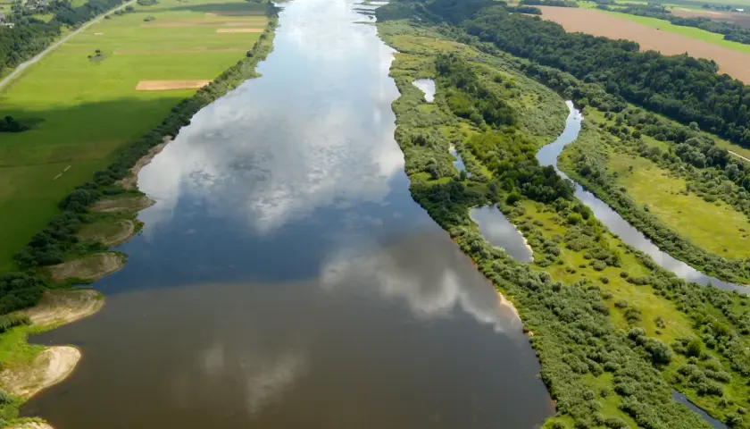 Szeroka rzeka Nemen meandruje przez zielone pola i lasy, odbijając chmury na swojej tafli.