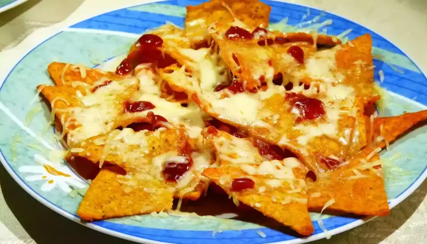 Nachos con queso derretido y salsa roja, servidos en un plato azul y verde. ¡Un antojo irresistible!