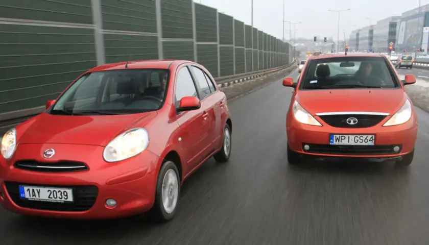 Dwa czerwone samochody, Nissan i tata indica, jadą obok siebie po mokrej drodze.